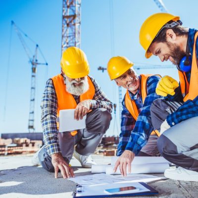 three-construction-workers-sitting-on-concrete-at-construction-site-discussing-building-plans.jpg